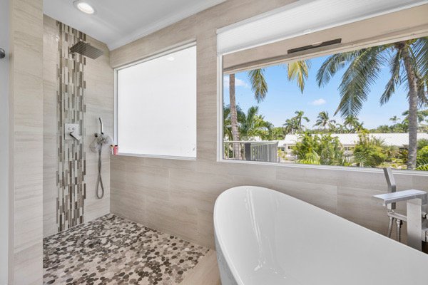 Indulge in luxury with this spa-inspired bathroom, boasting a walk-in rainfall shower, elegant soaking tub, and breathtaking tropical views for ultimate relaxation.